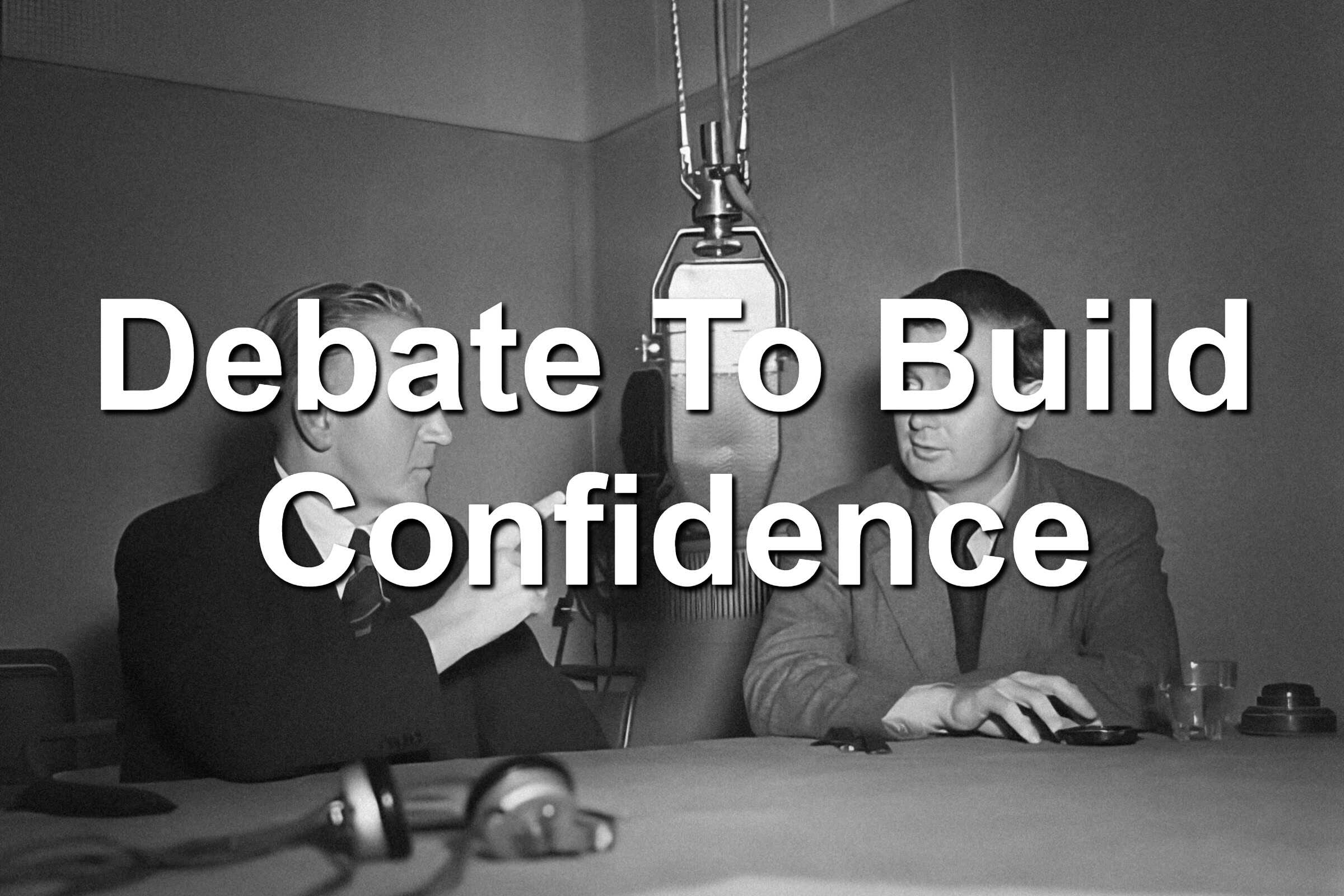 Two men sitting in front of a microphone. A debate is happening.