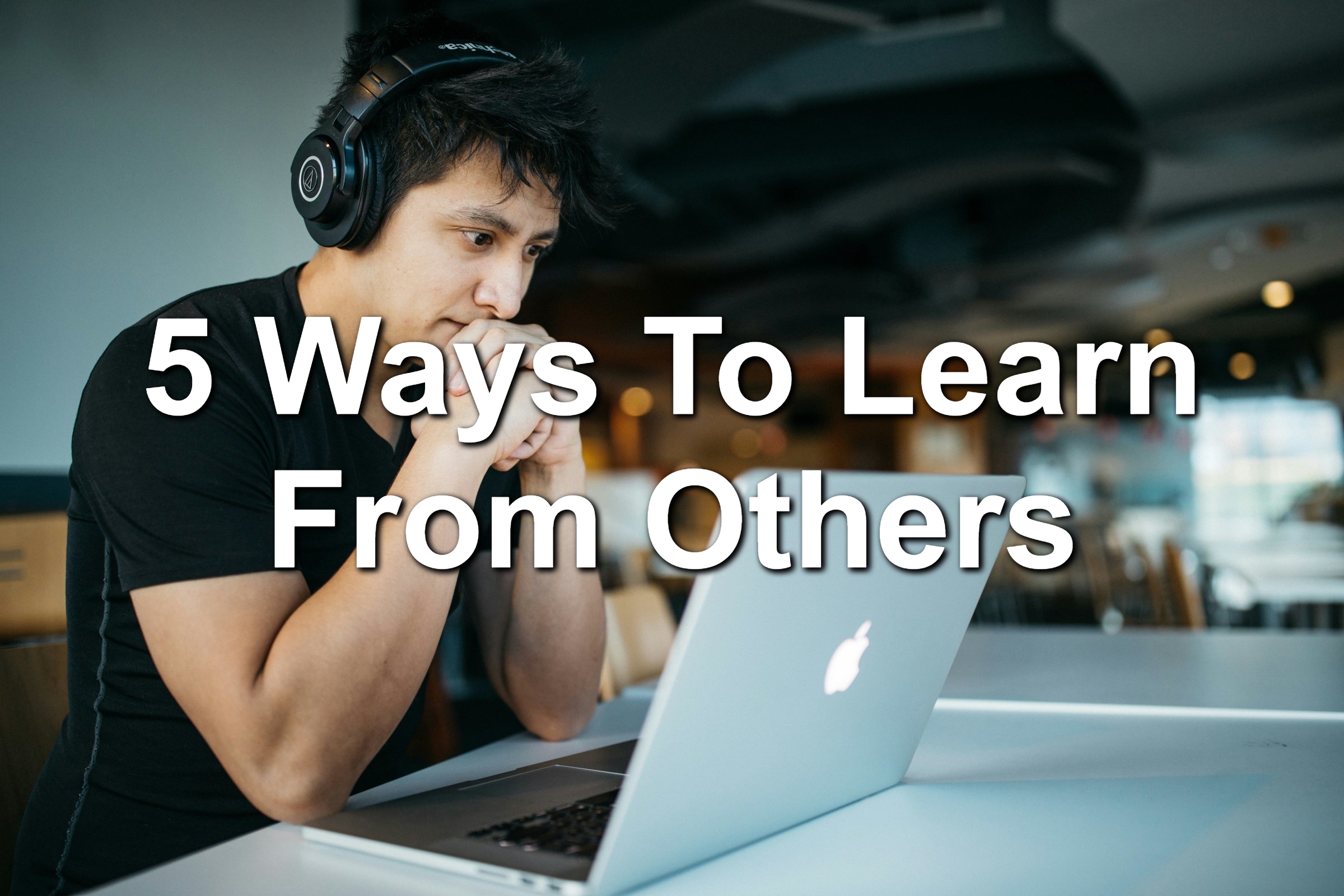Man sitting in front of a MacBook. He's wearing headphones and looks like he is learning.