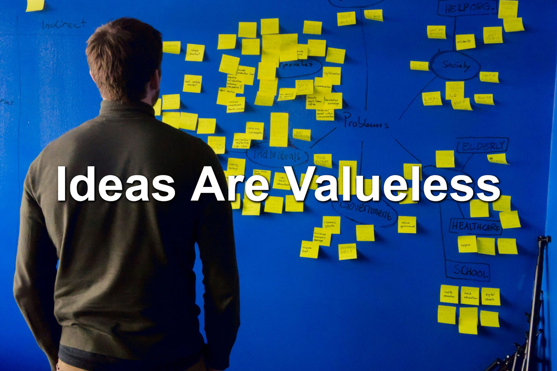 A man standing in front of a blue wall. Hundreds of yellow sticky notes are in front of him
