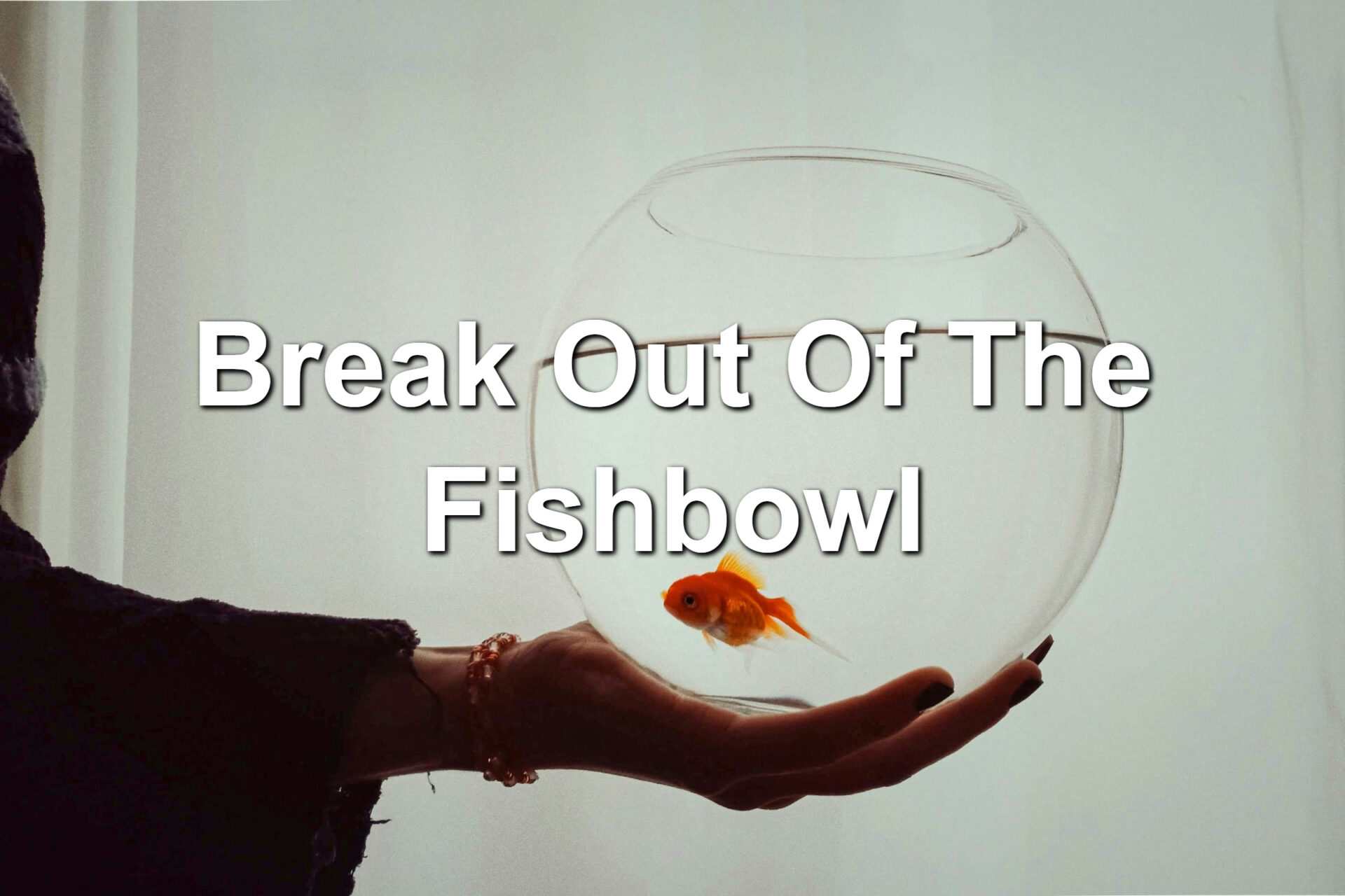 A person holding a fishbowl in one hand. There is a goldfish inside.